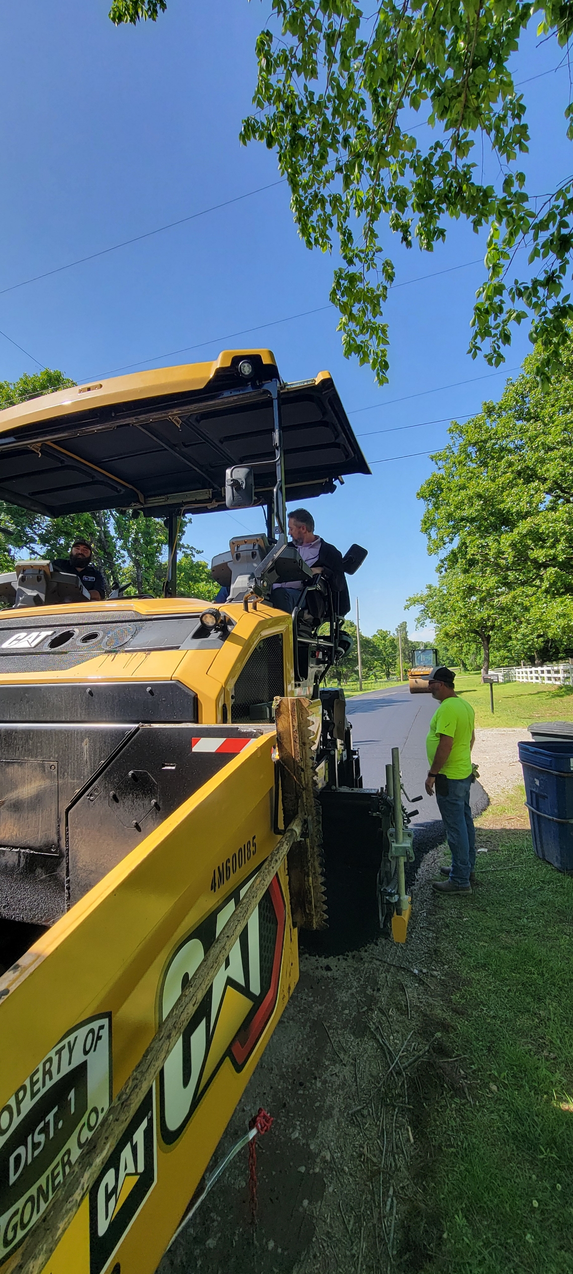 Commissioner Hanning at the controls of a CAT paver labeled 'Property of Dist 1, Wagoner Co.' on a District 1 road project